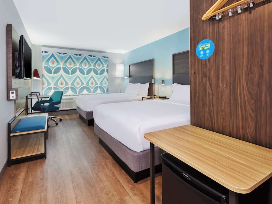 A hotel room with two beds, a desk, a chair, a TV, and a wall with a storage sign.