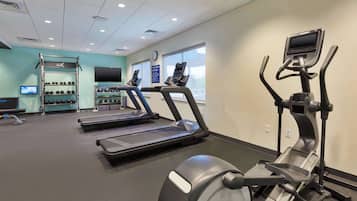 Un gimnasio con cintas de correr, una bicicleta estática y un soporte para pesas.