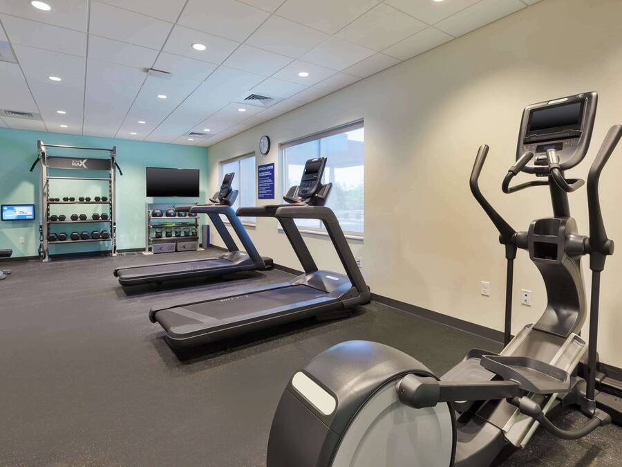 Un gimnasio con cintas de correr, una bicicleta estática y un soporte para pesas.
