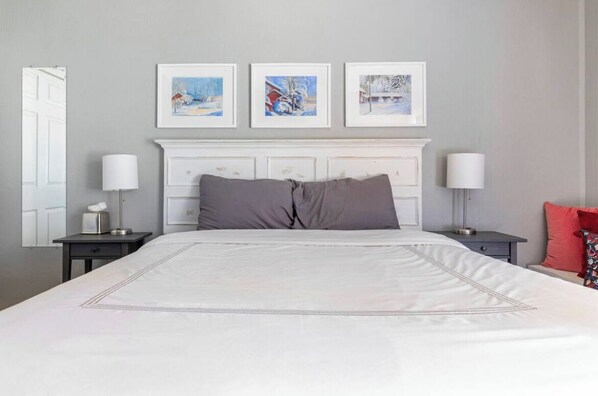 A neatly arranged bedroom with a large bed, white headboard, and three framed pictures above it.