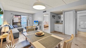 A modern, well-lit room with a dining table, chairs, a sofa, and a TV. - Ocean view condo with 2 pools, tennis and easy beach access (St. Augustine Beach)