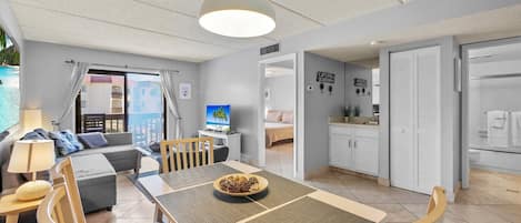 A modern, well-lit room with a dining table, chairs, a sofa, and a TV.