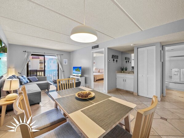 A modern, well-lit room with a dining table, chairs, a sofa, and a TV. - Ocean view condo with 2 pools, tennis and easy beach access (St. Augustine Beach)