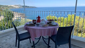 A table set for two with a pink tablecloth, two chairs, and a view of the sea.