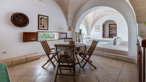 A dining area with a round table and four chairs, an arched ceiling, and a view into an adjacent room with a sofa.