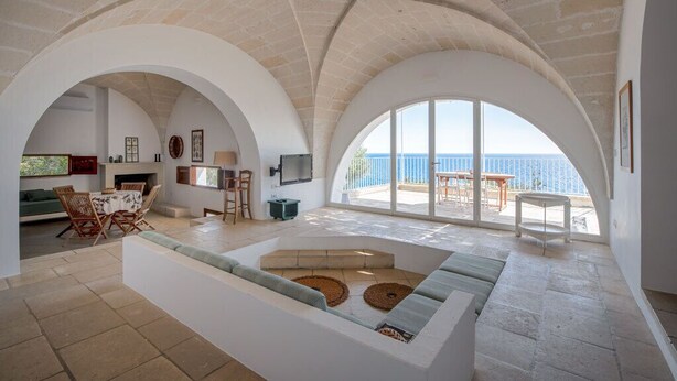 A spacious living area with a high arched ceiling, a large window overlooking the sea, and a cozy seating area with a fireplace.
