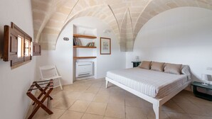 A bedroom with a bed, a chair, a small table, and a shelf with books and a picture frame.
