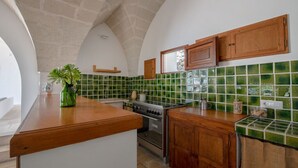 A kitchen with a stone arch ceiling, green tiled backsplash, wooden cabinets, and a central island with a vase.