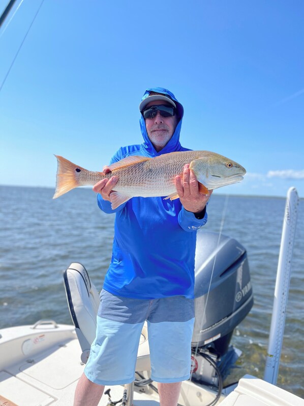 A person holding a fish on a boat with a Yamaha outboard motor.