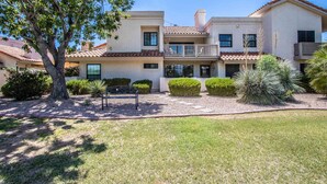 A two-story building with a flat roof, a balcony on the second floor, and a well-maintained lawn with trimmed bushes and a tree. - Mountain Views and walk out to Silverado golf course and greenbelt by Old Town (Scottsdale)