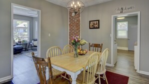 A dining area with a wooden table, six chairs, a chandelier, and a brick accent wall. - Charm Near Omaha Downtown: 4-Bed, 2-Bath Gem (Omaha)