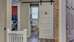 A hallway with a wooden floor, a white door with a black handle, and a ceiling light fixture. - Charm Near Omaha Downtown: 4-Bed, 2-Bath Gem (Omaha)