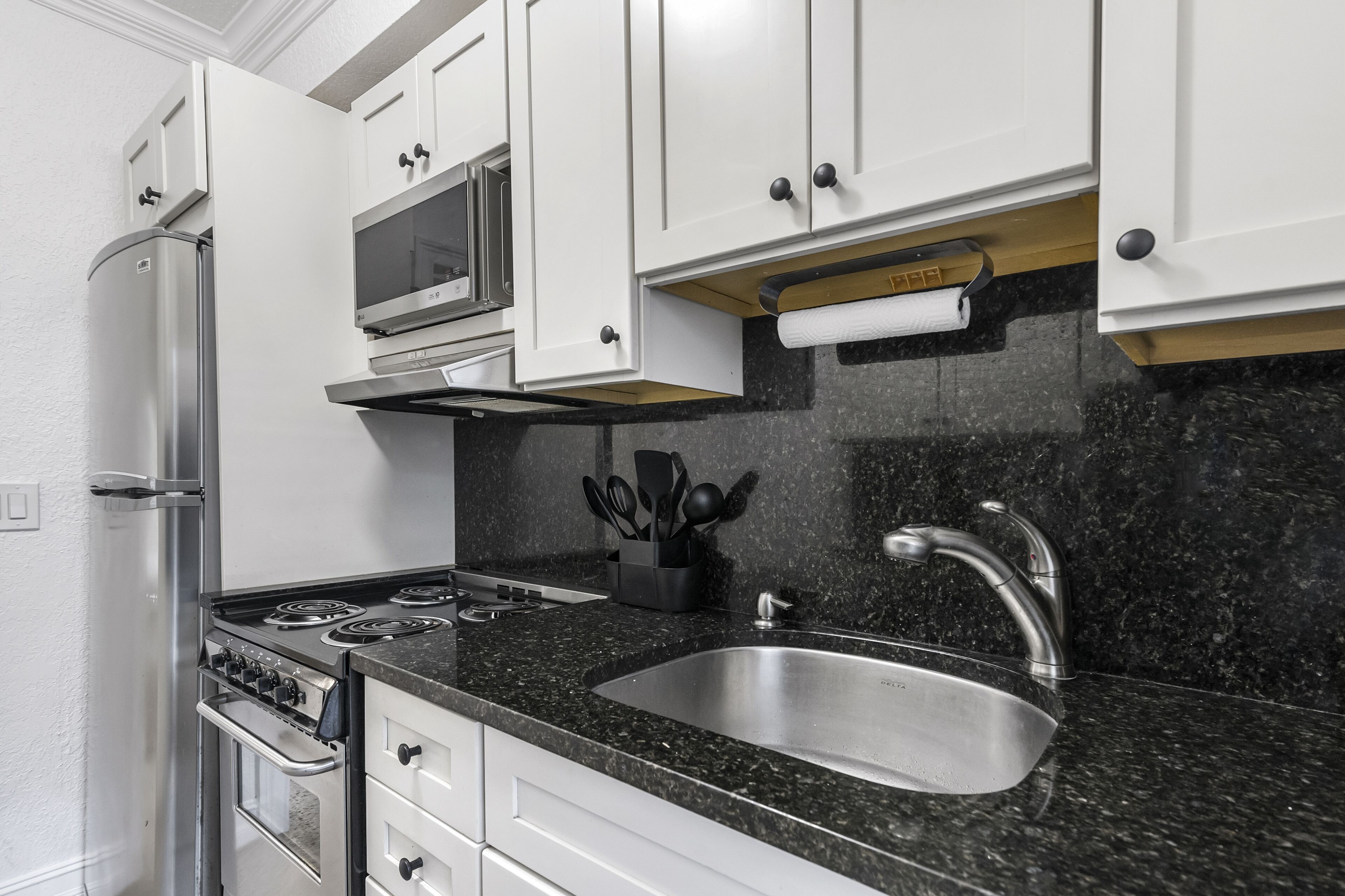 A kitchen with white cabinets, a stainless steel sink, a microwave, and a gas stove.