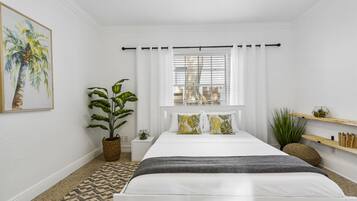 A bedroom with a bed, a window with blinds, a ceiling fan, a potted plant, and a wall-mounted shelf.