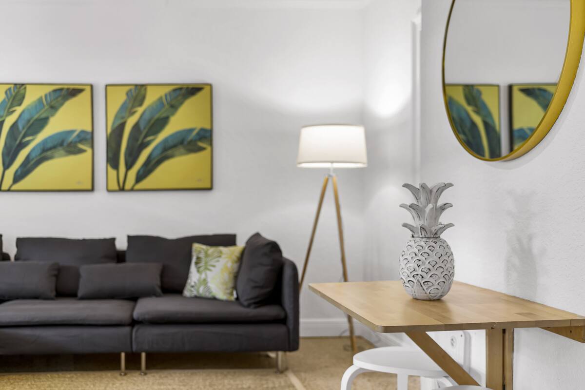 Ein modernes Wohnzimmer mit einem dunkelgrauen Sofa, einem weißen Sessel, einem Holztisch, einer Stehlampe und zwei Wandgemälden.