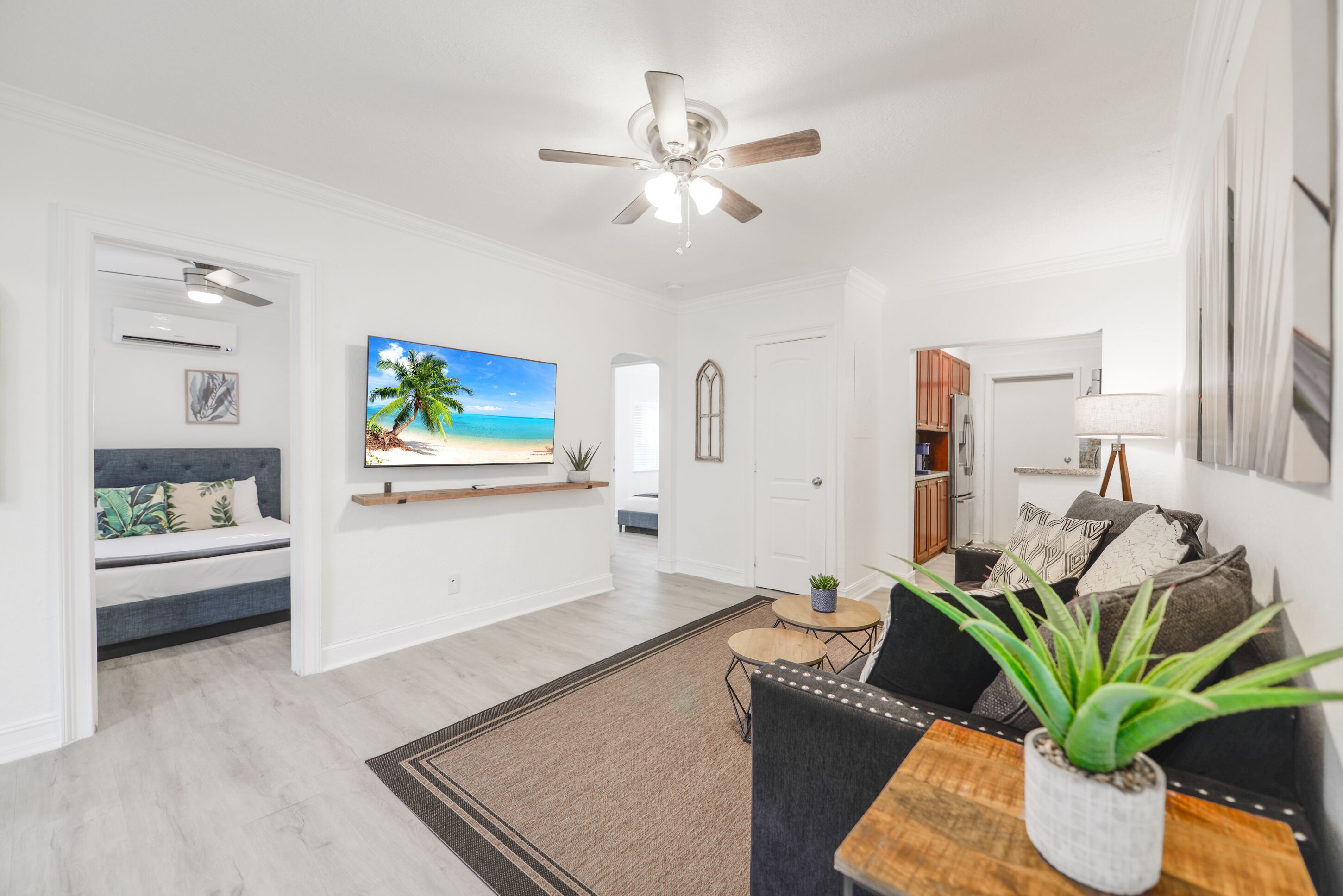 A modern living room with a ceiling fan, a flat-screen TV, a sofa, a coffee table, and a dining table.