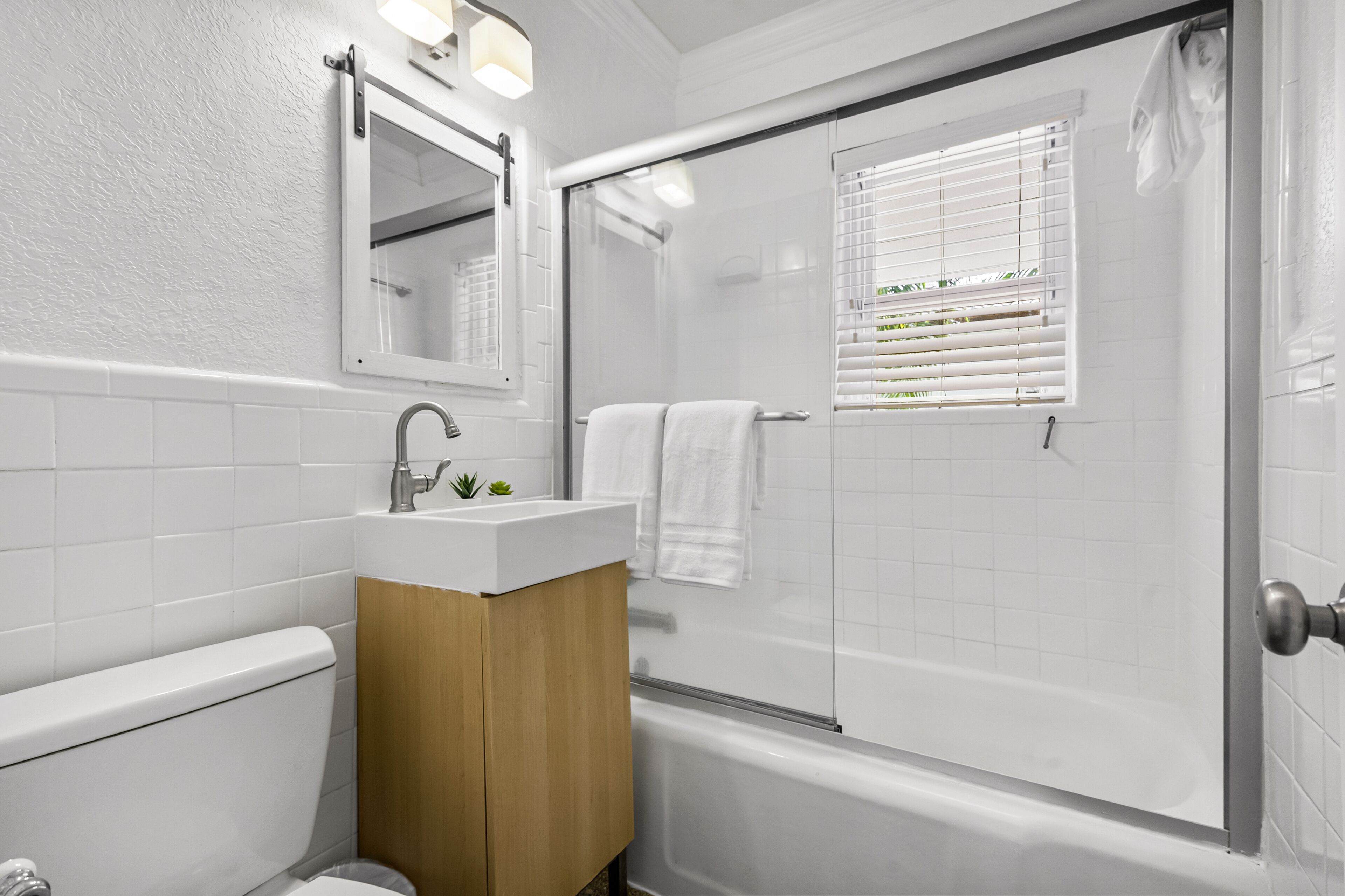 A modern bathroom with a white sink, wooden vanity, a glass shower enclosure, and a bathtub.