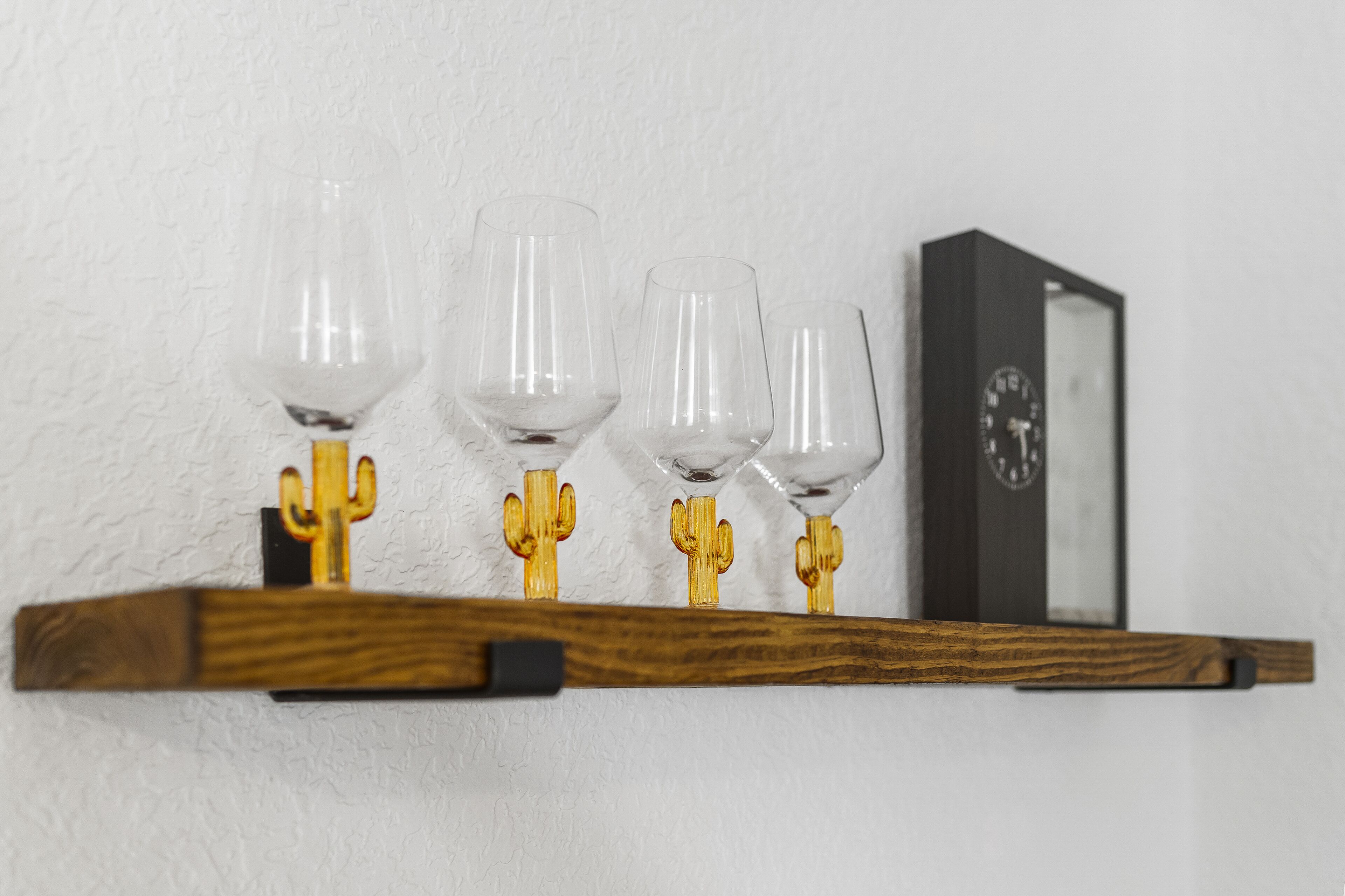 Una estantería de madera con cuatro copas de vino y un reloj.