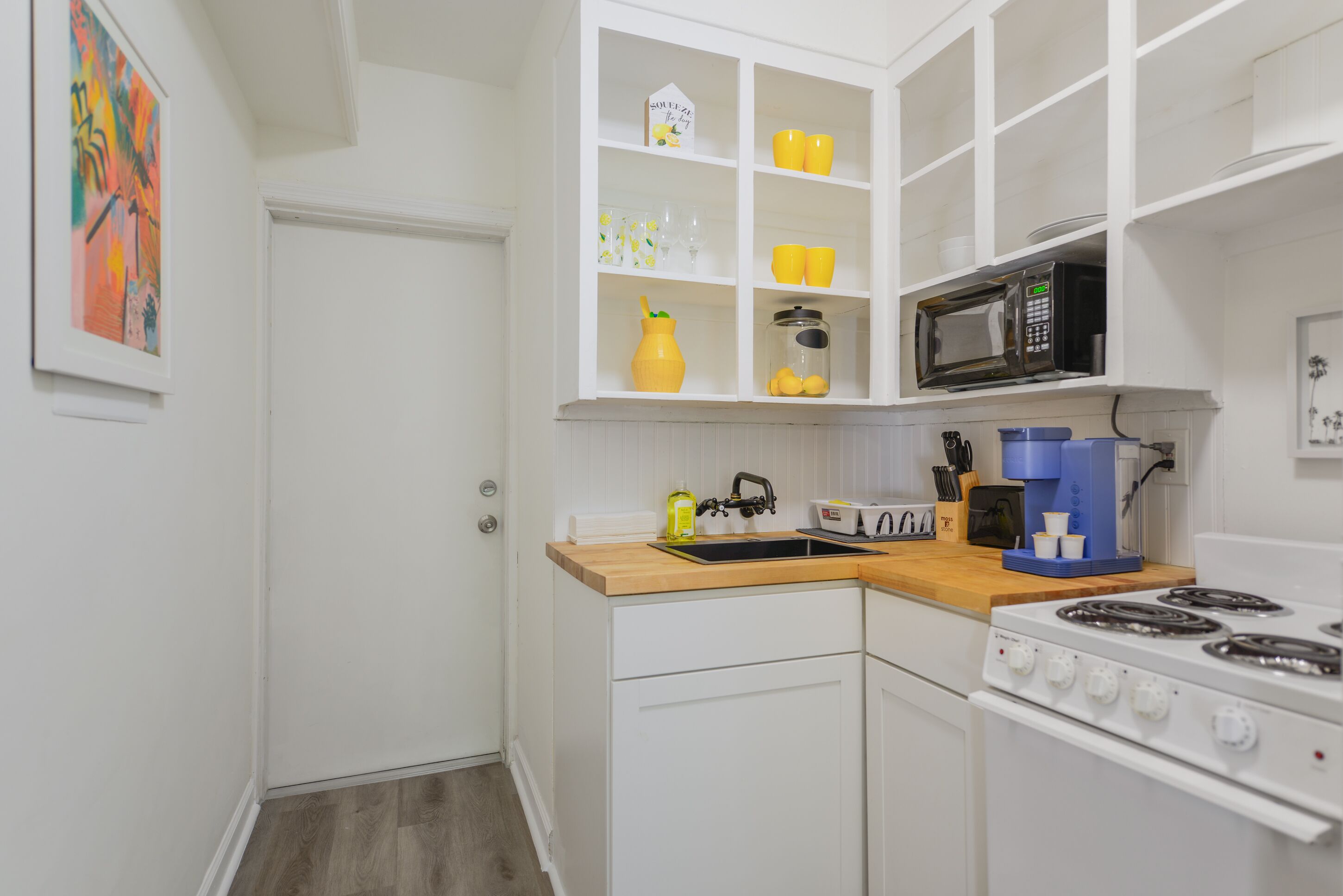 A compact kitchen with white cabinetry, a microwave, a stove, and a wooden countertop.