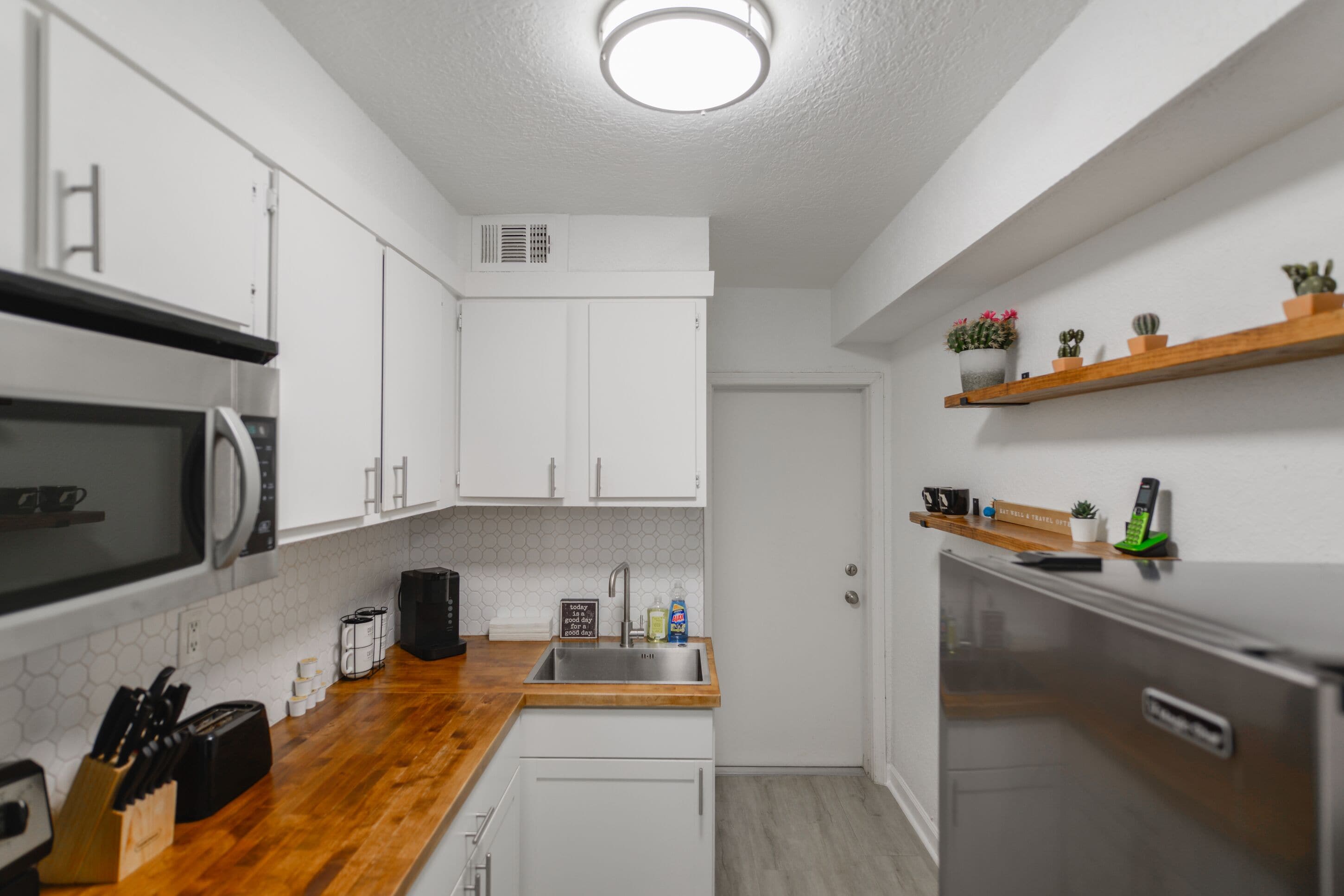 A compact kitchen with white cabinets, a wooden countertop, a stainless steel refrigerator, and a microwave.