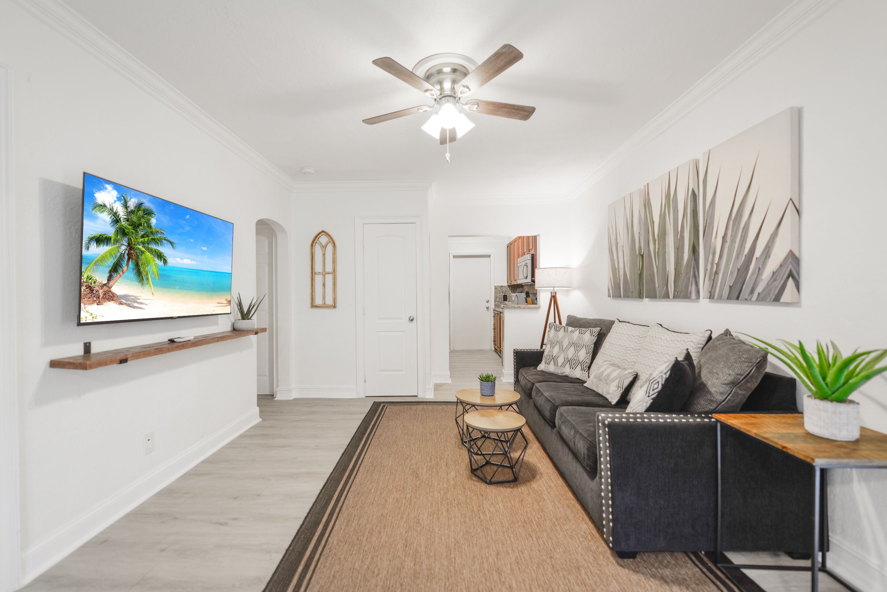 A modern living room with a flat-screen TV, a ceiling fan, and a large abstract painting.