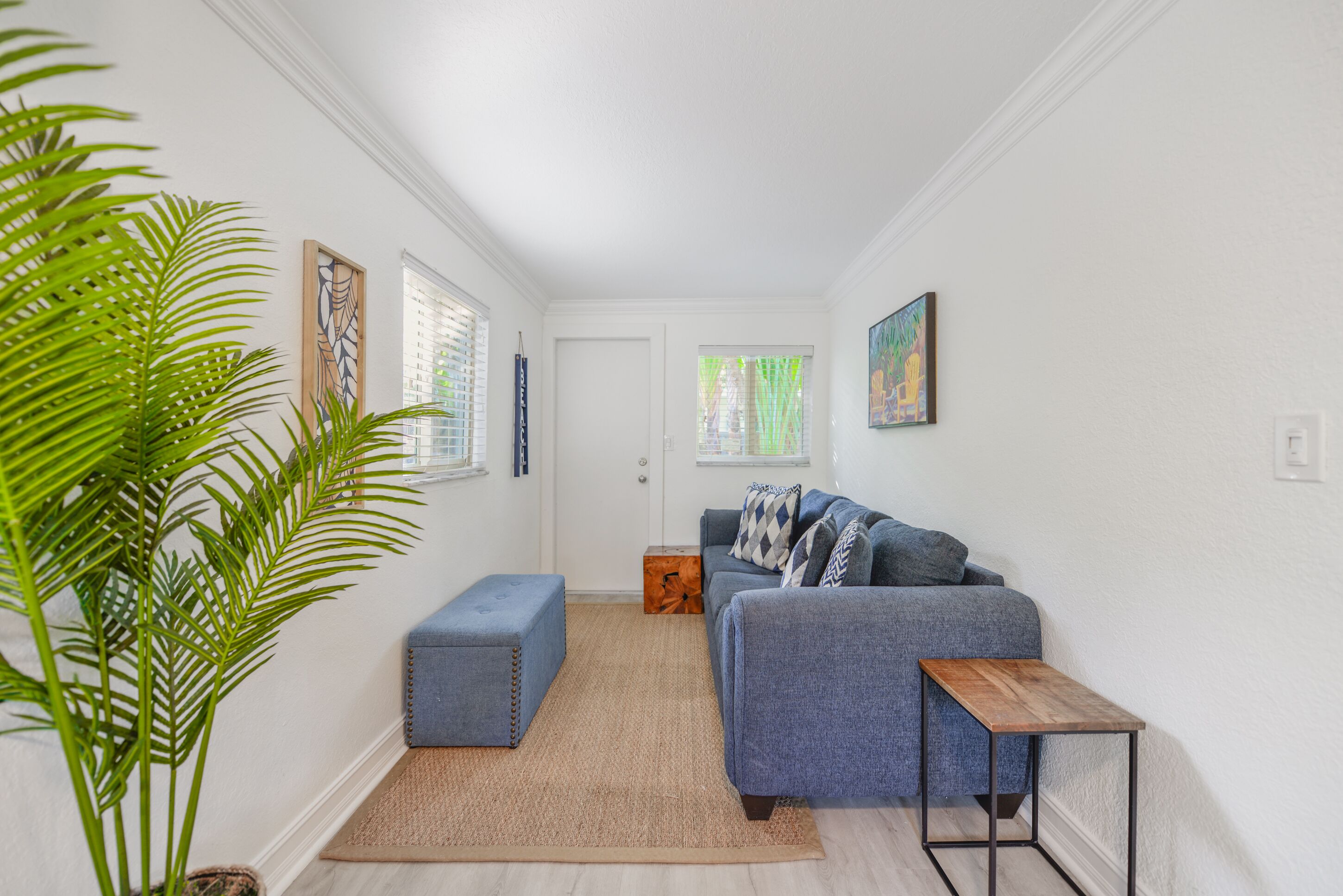 Una sala moderna con un sofá gris, una mesa de centro de madera y una planta verde grande.