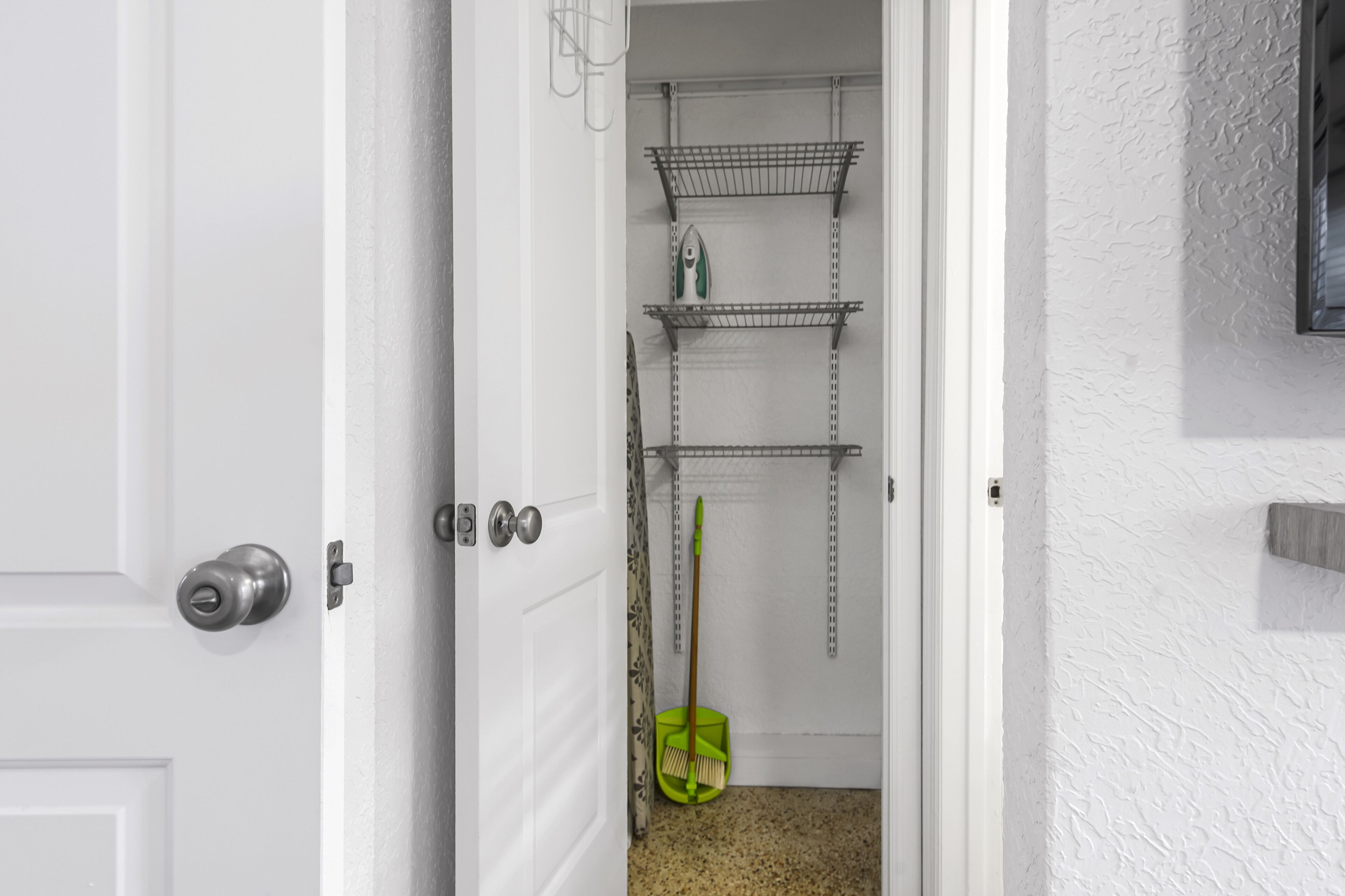 A narrow hallway with a white door, a broom, and metal shelves against the wall.