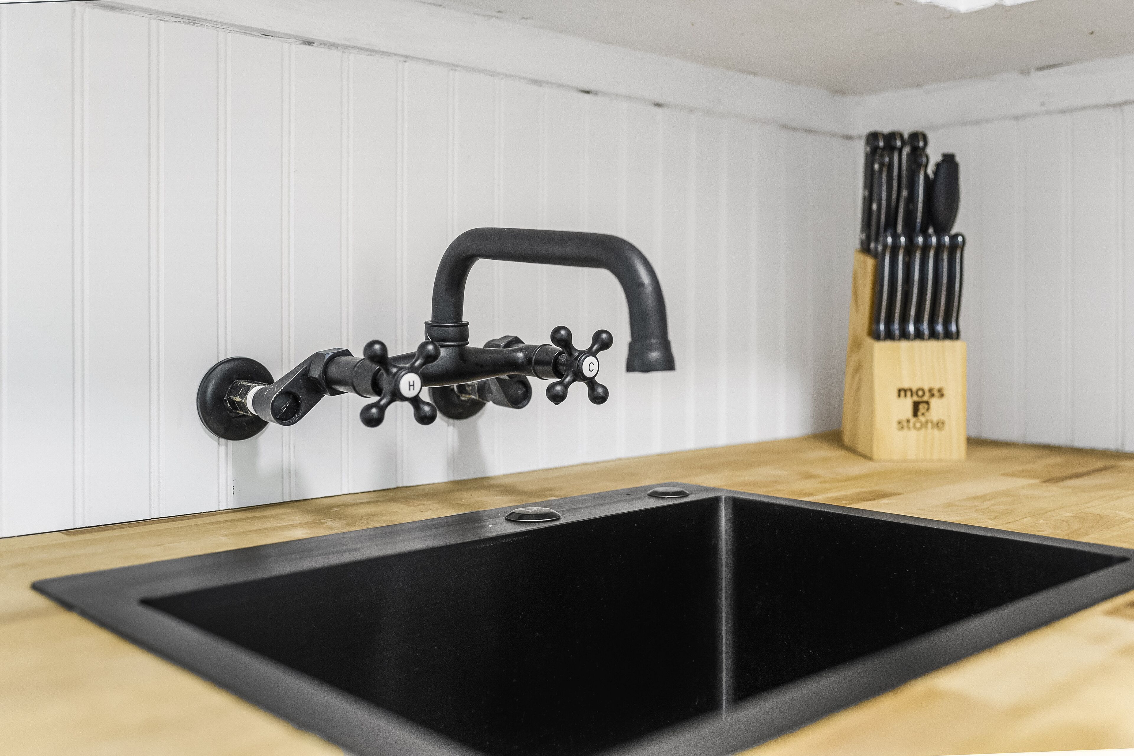 A kitchen with a black sink, a faucet with multiple handles, and a knife block on the countertop.