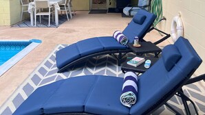 Een overdekt terras met loungezetels, een zwembad en een tafel met stoelen.