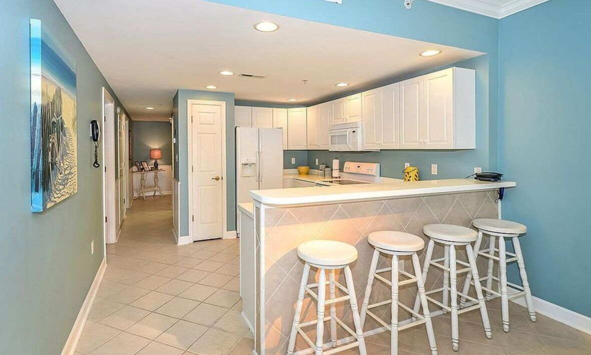 Una cocina moderna con armarios blancos, una isla central con taburetes y vistas al área de estar contigua.