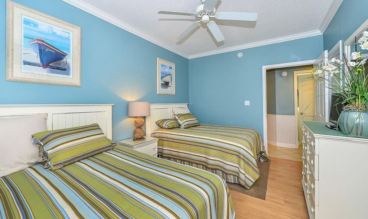Une chambre avec deux lits, un ventilateur de plafond et des œuvres d’art accrochées aux murs.