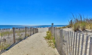 A sandy beach path with a wooden fence on one side and a metal fence on the other, leading to the beach.