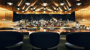 A bar with a variety of bottles and glasses, a bar counter, and three chairs in the foreground. - Kinley Chattanooga Southside, a Tribute Portfolio Hotel (Chattanooga)