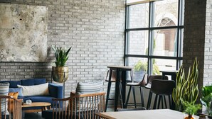 A modern living room with a brick wall, a large window, and a blue sofa. - Kinley Chattanooga Southside, a Tribute Portfolio Hotel (Chattanooga)