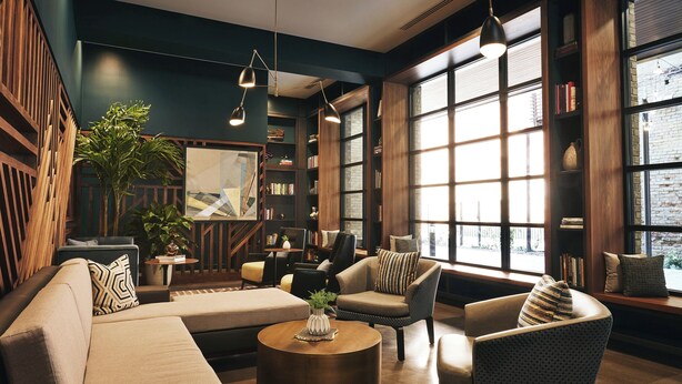 A cozy lounge area with sofas, armchairs, and a coffee table, surrounded by bookshelves and large windows. - Kinley Chattanooga Southside, a Tribute Portfolio Hotel (Chattanooga)