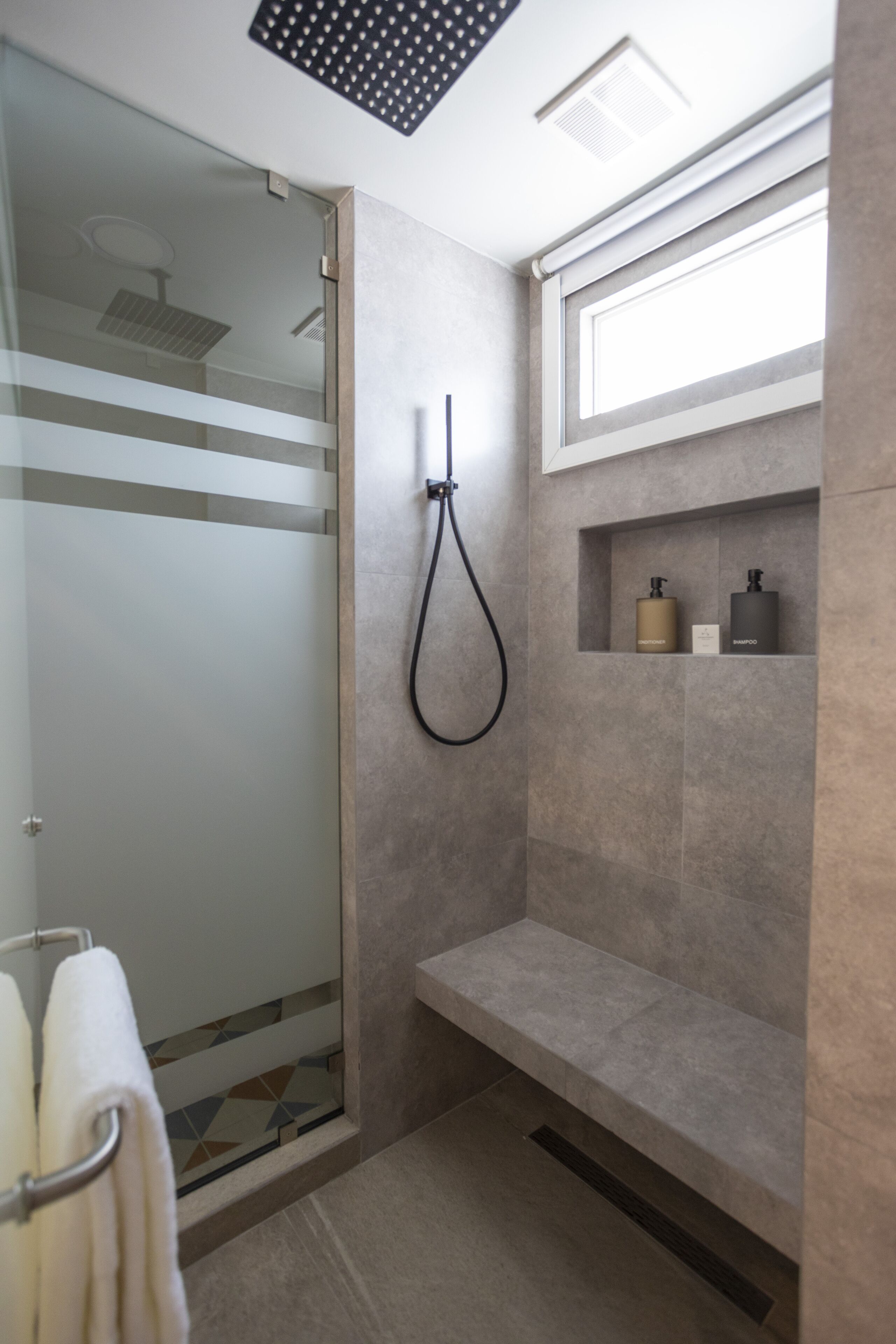 Een moderne badkamer met een douchecabine van glas, een inbouwkruk en een plank met toiletartikelen.