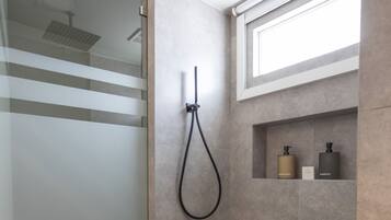 Een moderne badkamer met een douchecabine van glas, een inbouwkruk en een plank met toiletartikelen.