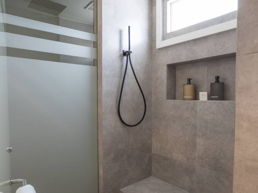 Een moderne badkamer met een douchecabine van glas, een inbouwkruk en een plank met toiletartikelen.