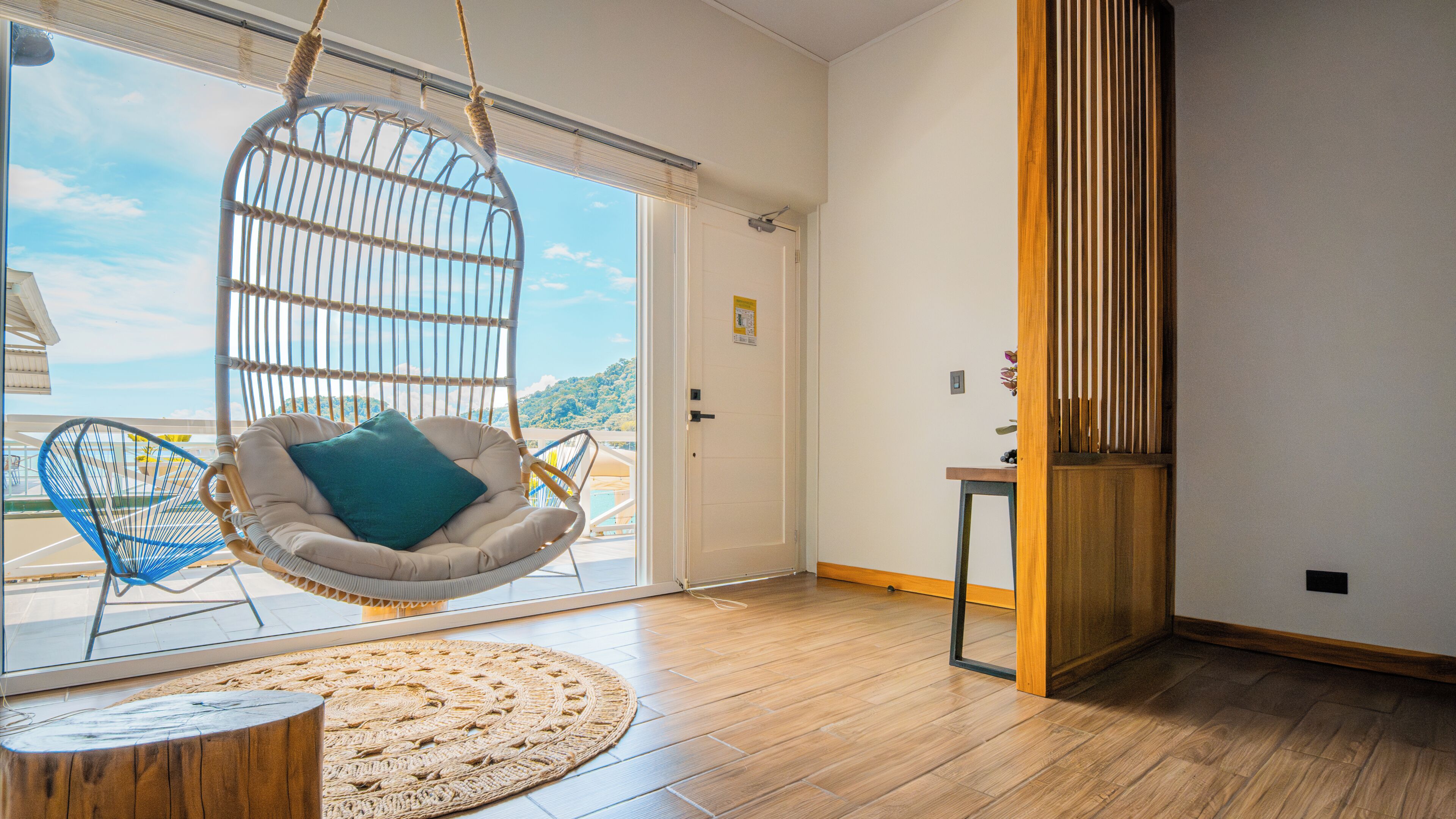 Una habitación con una silla colgante, una mesita, suelo de madera y una puerta que da al exterior.