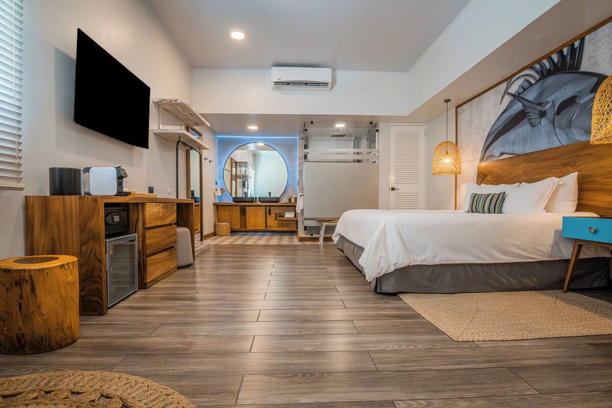 Habitación de hotel moderna con una cama, un televisor de pantalla plana, un aparador de madera, un escritorio y un espejo grande.