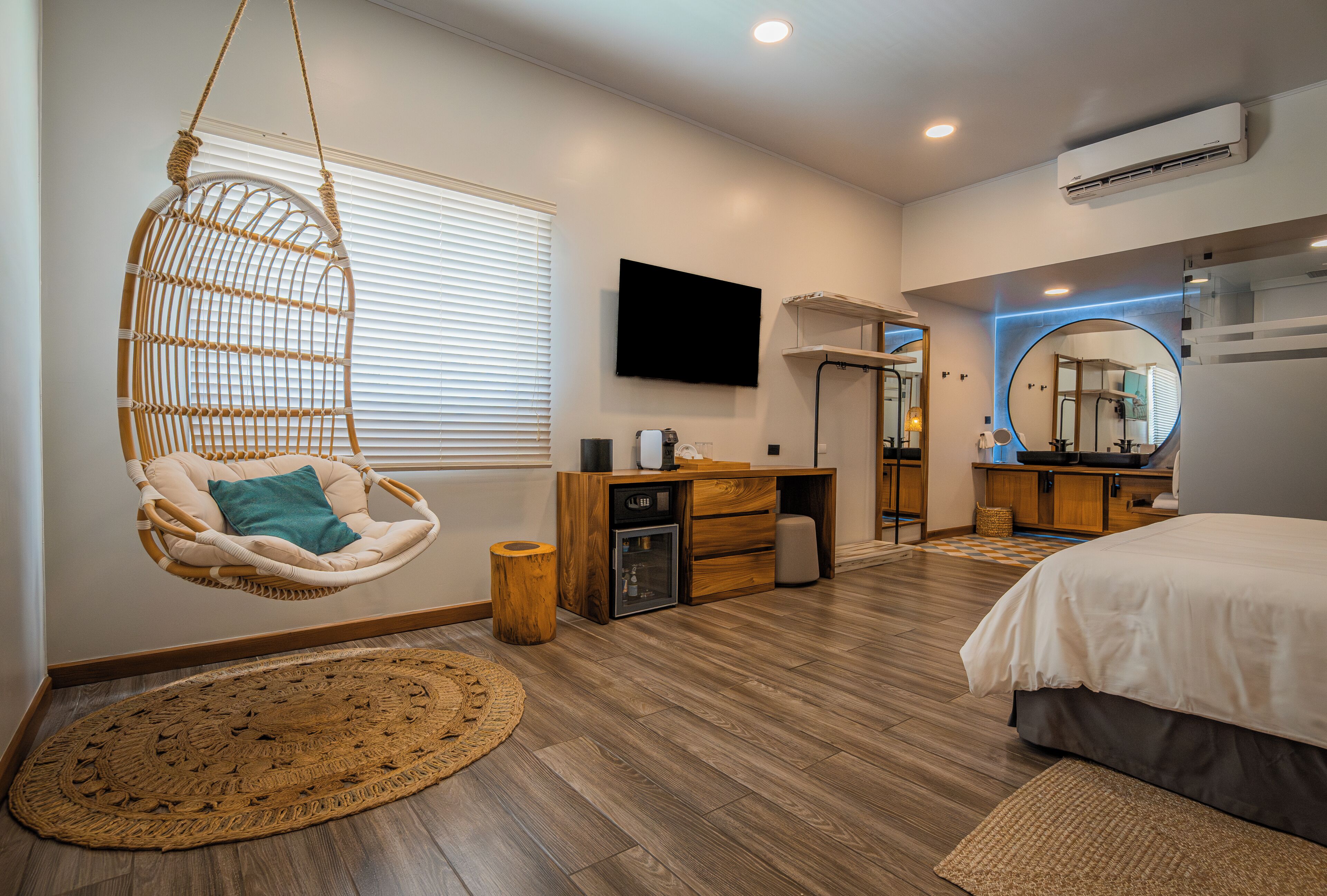 A modern bedroom with a hanging chair, a desk, a bed, and a television.
