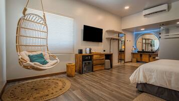 A modern bedroom with a hanging chair, a desk, a bed, and a television.
