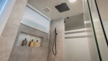 A modern shower area with a handheld showerhead, a built-in shelf with toiletries, and a ceiling vent.