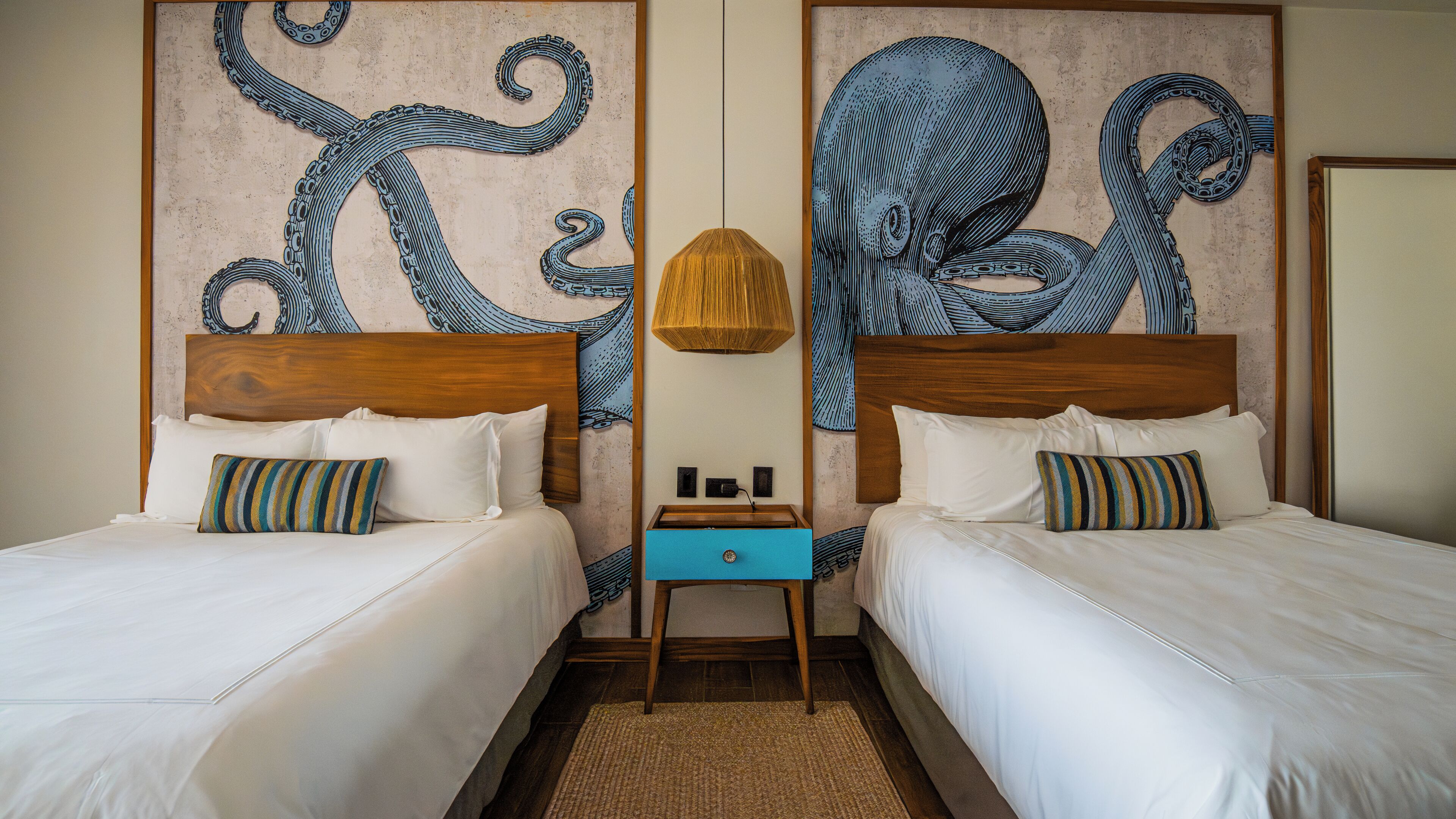 A hotel room with two beds, a wooden headboard, a small nightstand, and a wall mural of an octopus.
