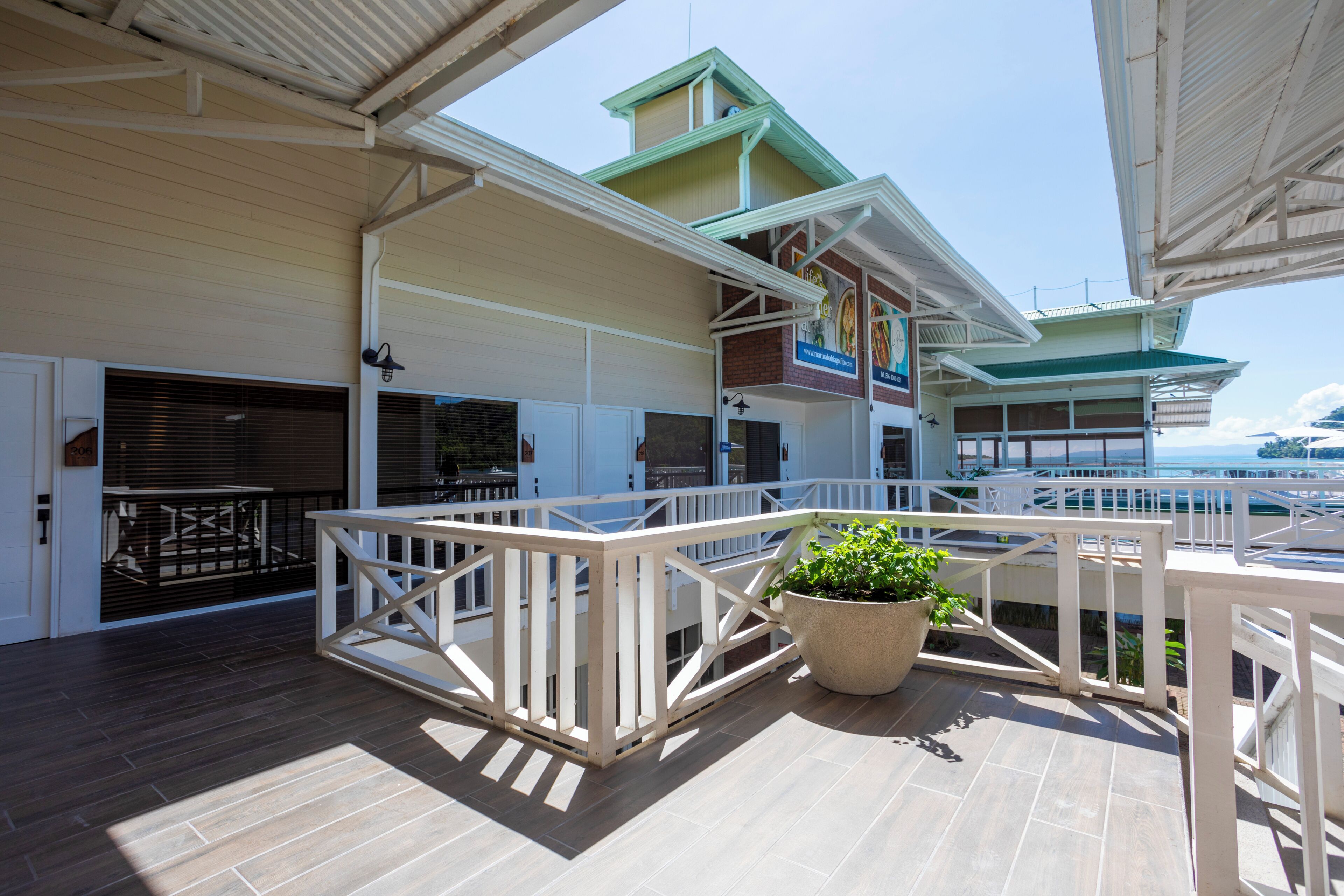 A covered outdoor deck with a railing, a potted plant, and a view of the sea.