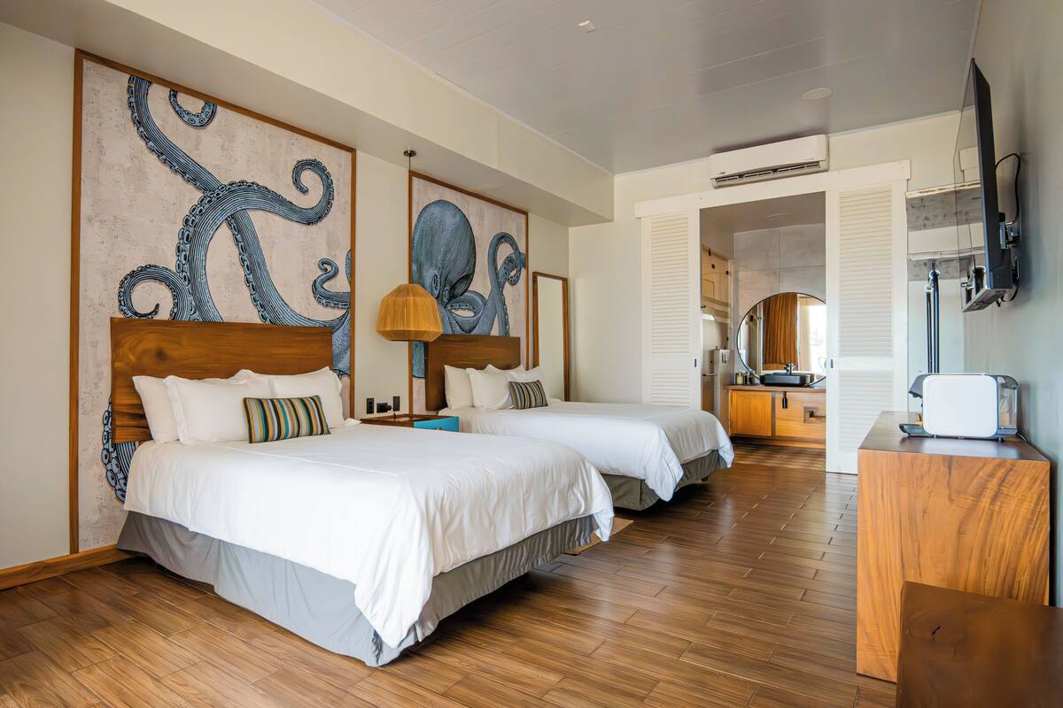 Habitación de hotel con dos camas, suelo de madera y un gran mural de pulpo en la pared.