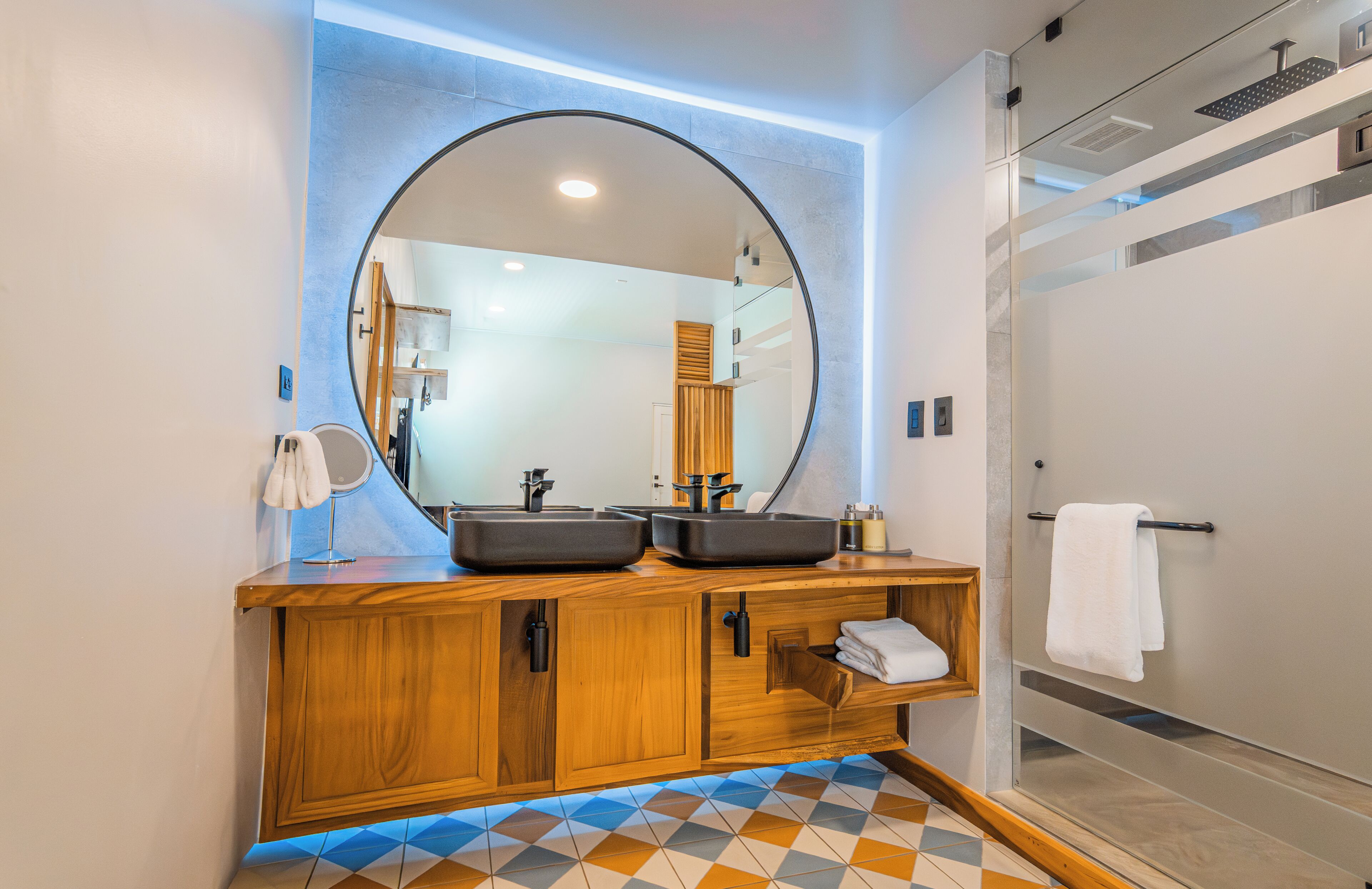 Un baño moderno con tocador de madera, dos lavamanos, un espejo grande y una cabina de ducha de vidrio.