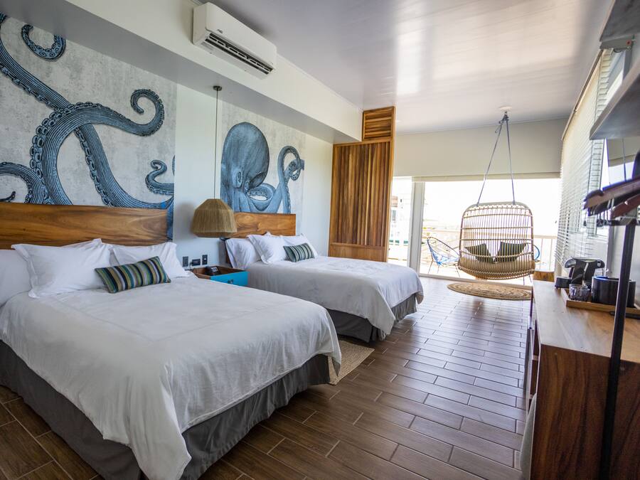 A hotel room with two beds, wooden headboards, and a large octopus mural on the wall.