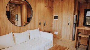 Ein Zimmer mit Holzwand, einem runden Spiegel, einem weißen Sofa, einem kleinen Holztisch und einem Kühlschrank.