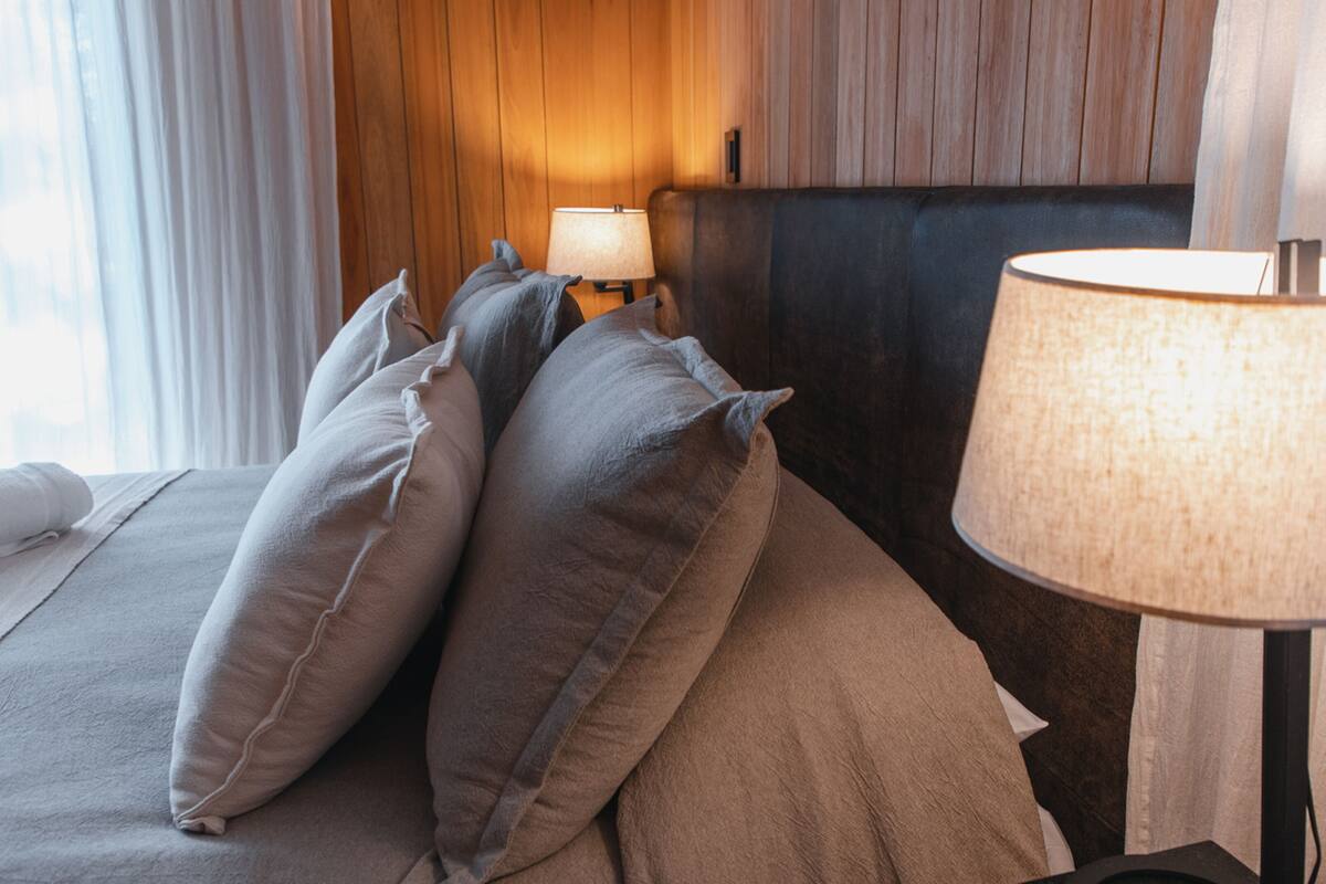 Un lit bien fait, avec des oreillers, une lampe de chevet et une tête de lit en bois.